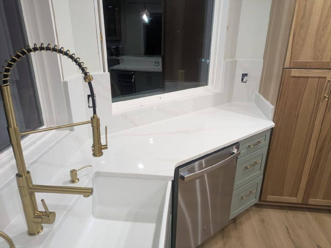 Accessible kitchen sink and countertop with gold faucet, window, and stainless dishwasher.