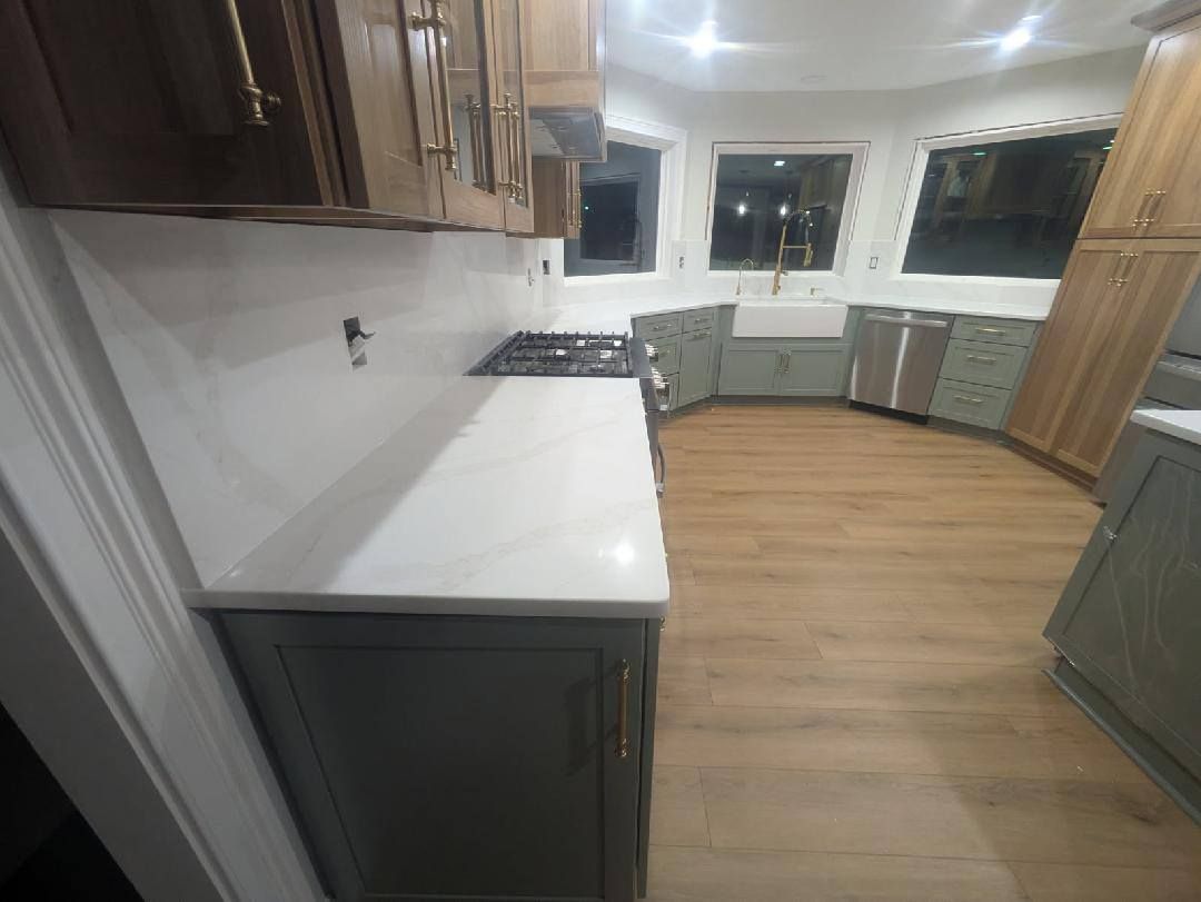Modern kitchen with dark cabinets, white countertops, wood floors, and bright windows.