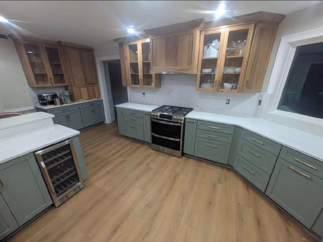 Spacious kitchen with green cabinets, wood floors, black stove, and large window.
