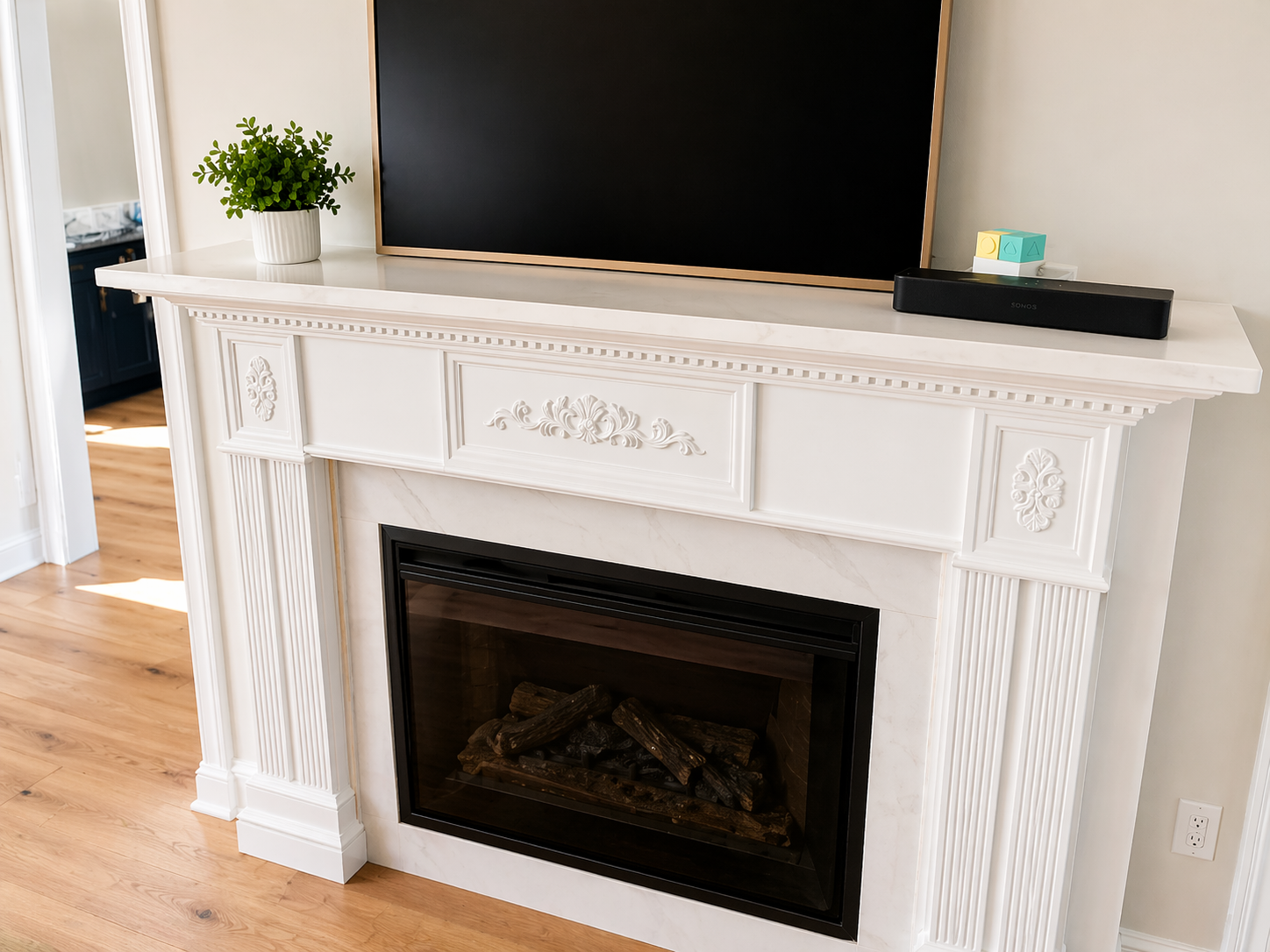 White carved fireplace mantel with a black TV above and a small plant on the left.