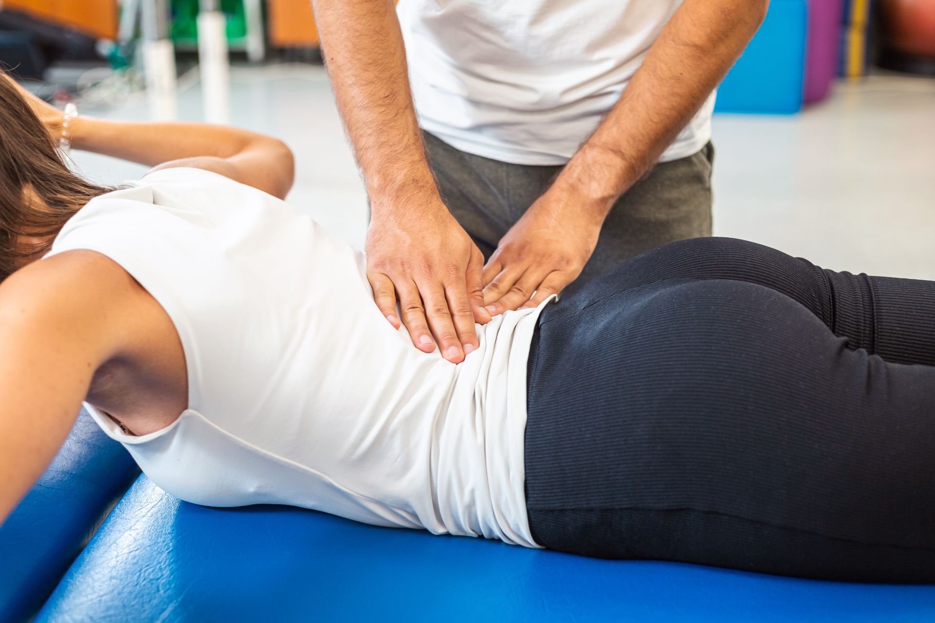 Physical therapist performing lower back treatment on a patient lying on a blue mat