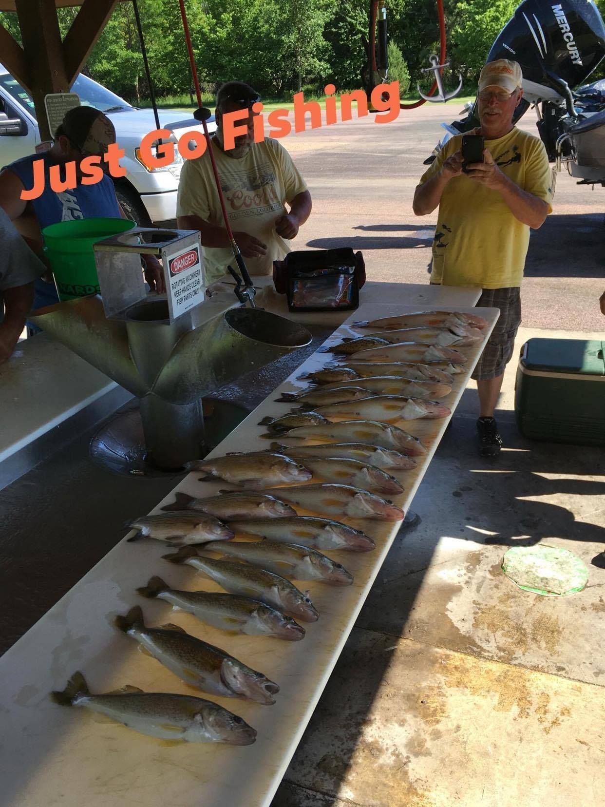 People display a long row of caught fish on a table at a lakeside spot with
