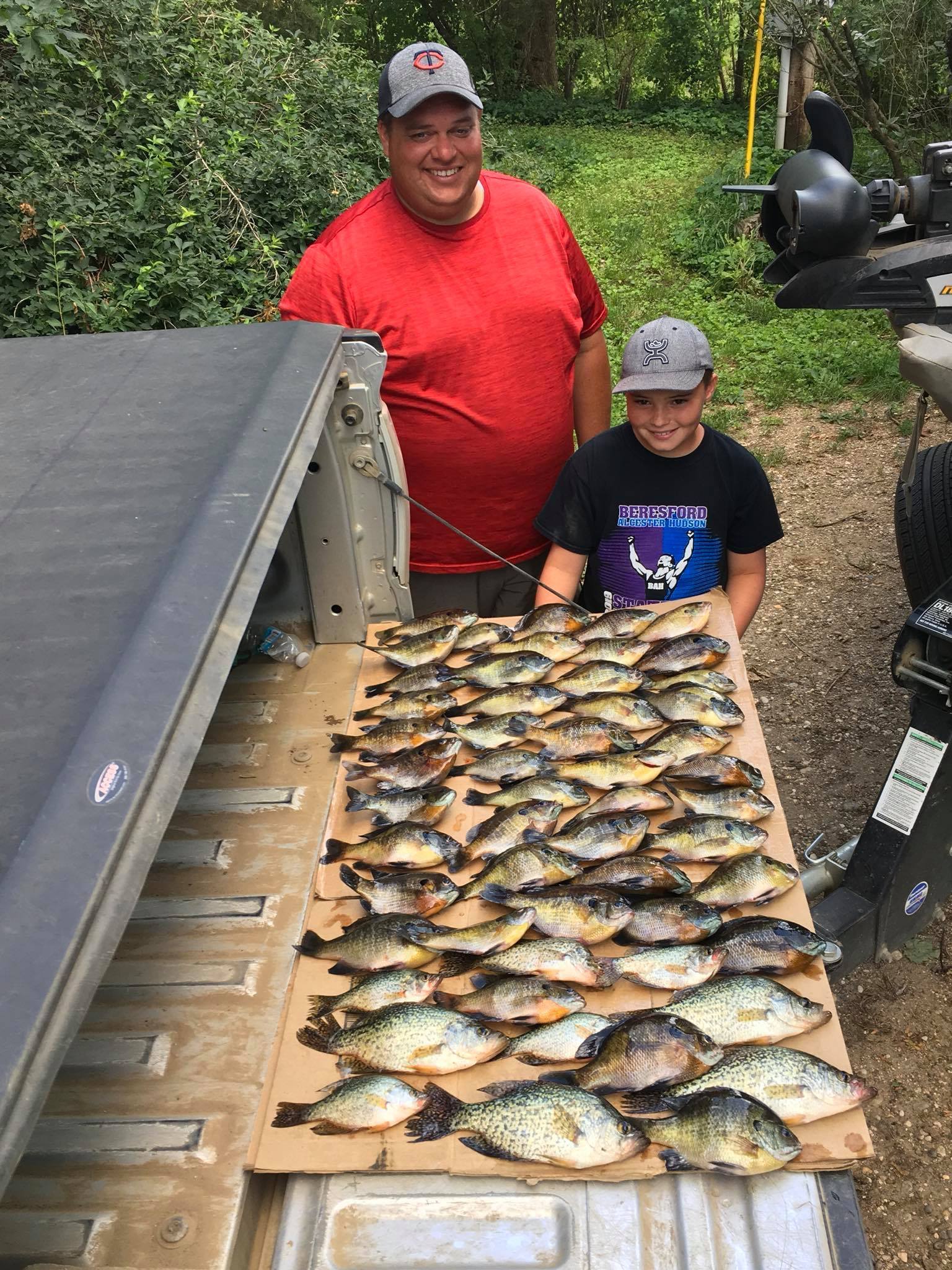 Man and child pose with a large catch of fish laid out on a truck bed.