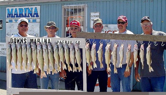 Men pose with a large catch of fish hanging from a rack in front of a marina.