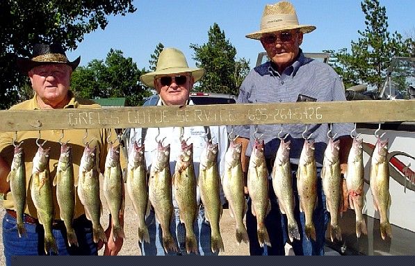 Three men holding up a wooden rack with many fish, likely a fishing catch, outdoors.