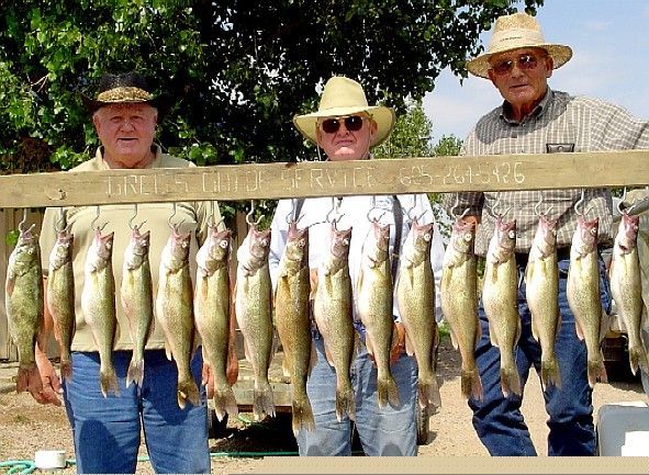 Three men in hats holding up a string of caught fish outdoors.