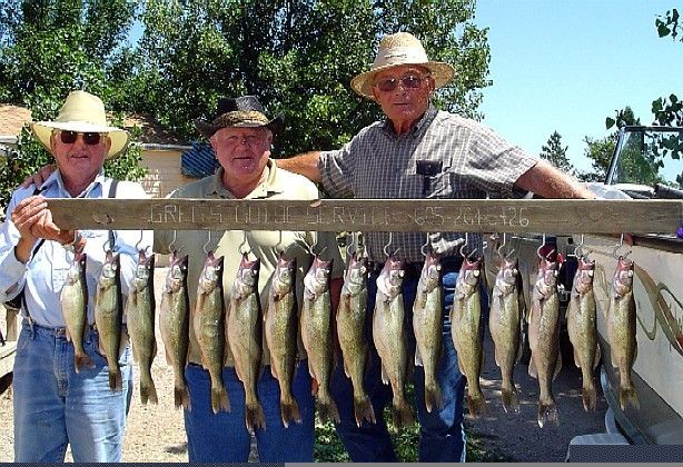 Three men display a stringer of fish, smiling in front of a boat on a sunny day.
