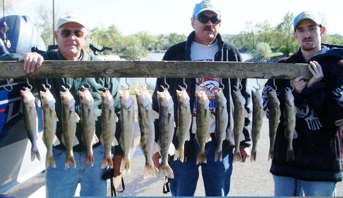Three men display a string of caught fish, near a boat on a sunny day.