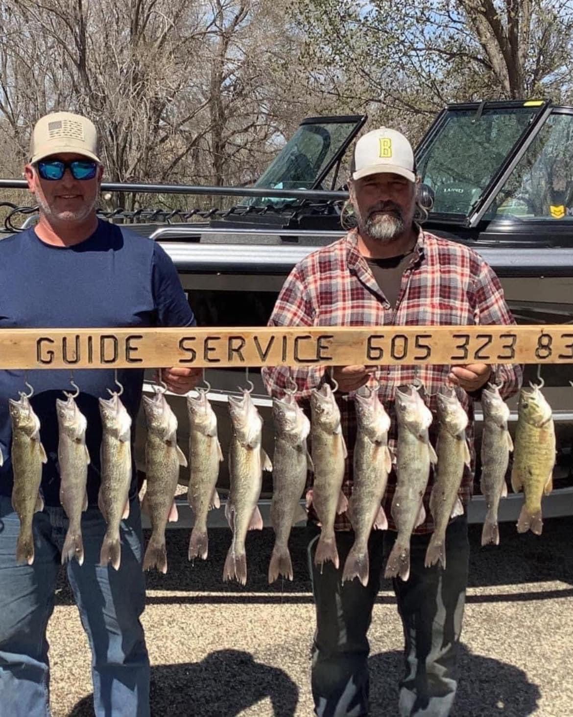 Two men holding up a board with Adams guide service number, displaying a string of caught walleye.