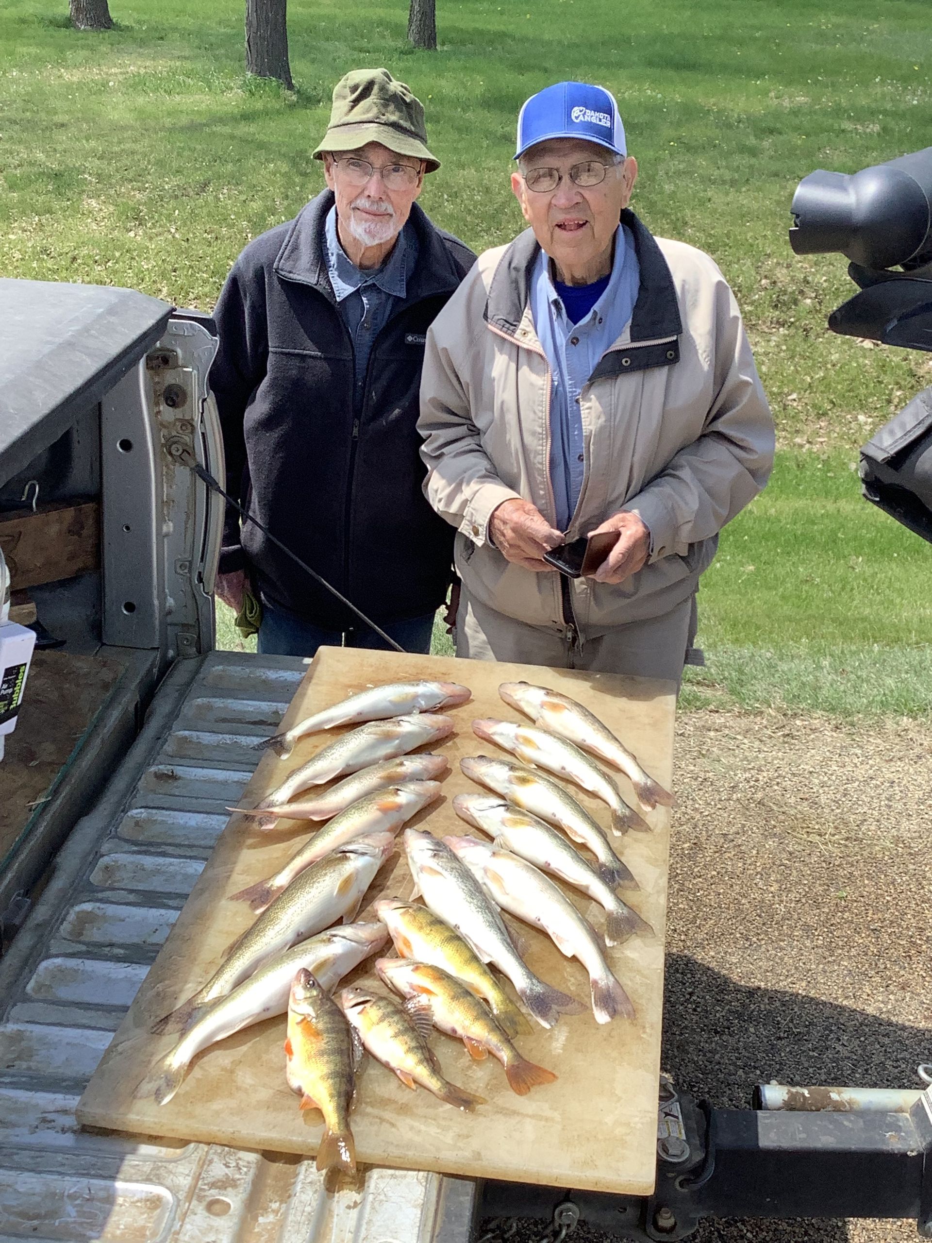 Two men standing near a truck with a catch of fish on a board, outdoors.
