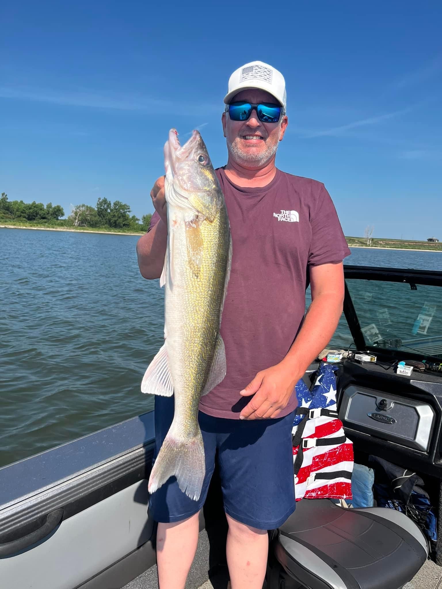 Man on boat holding large walleye fish on sunny day.