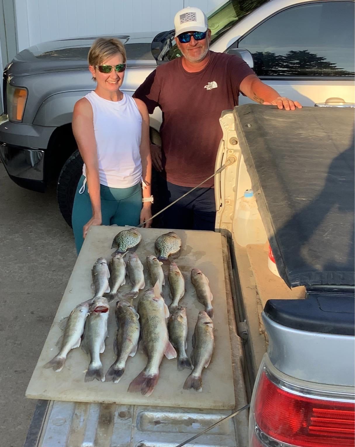 Couple with a fish catch on a cutting board, resting on a truck bed.