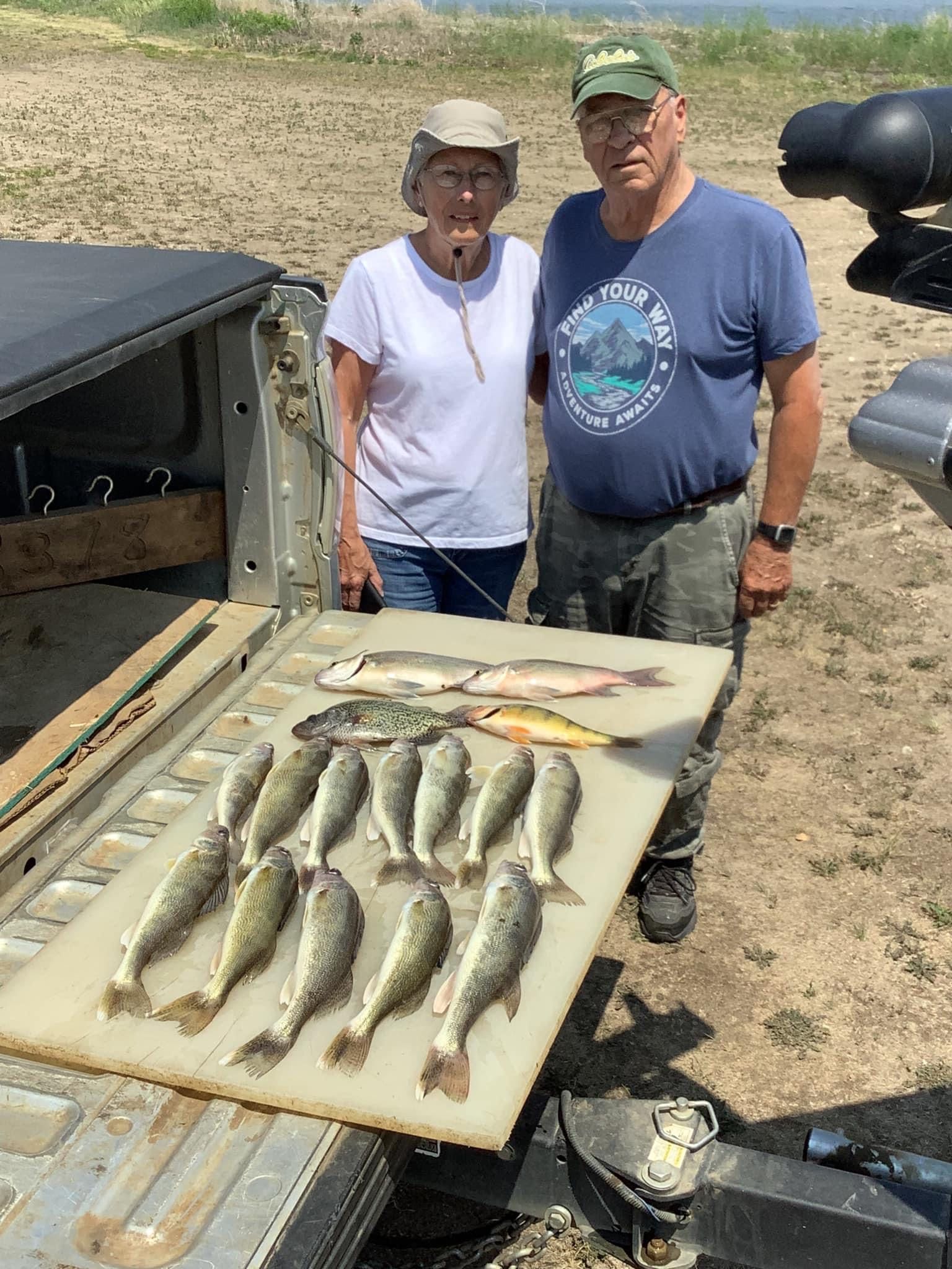 Couple stands with a large catch of fish on a tailgate, overlooking a lake.