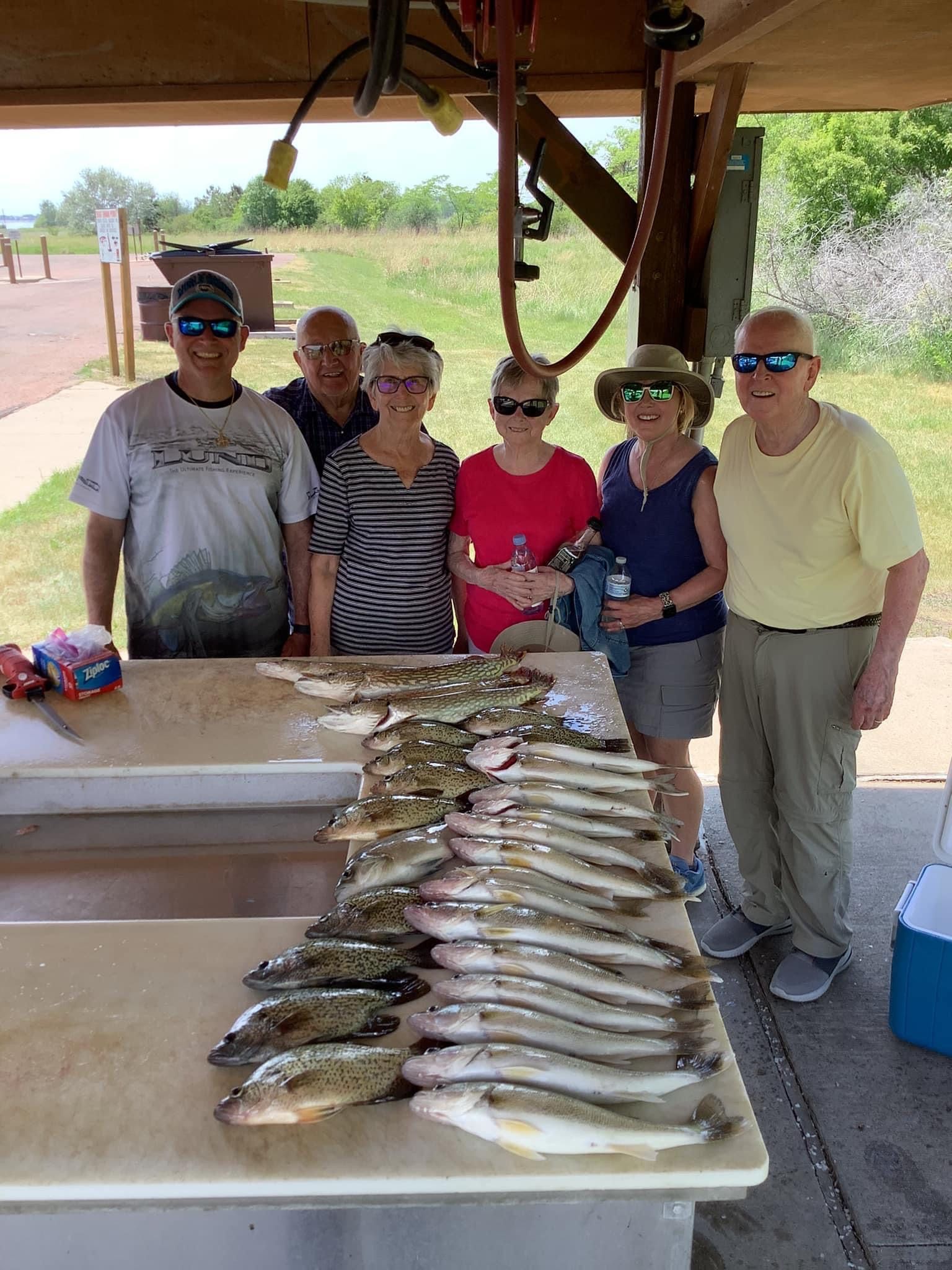 Group of people with a large catch of fish on a cleaning table. Outdoor setting.