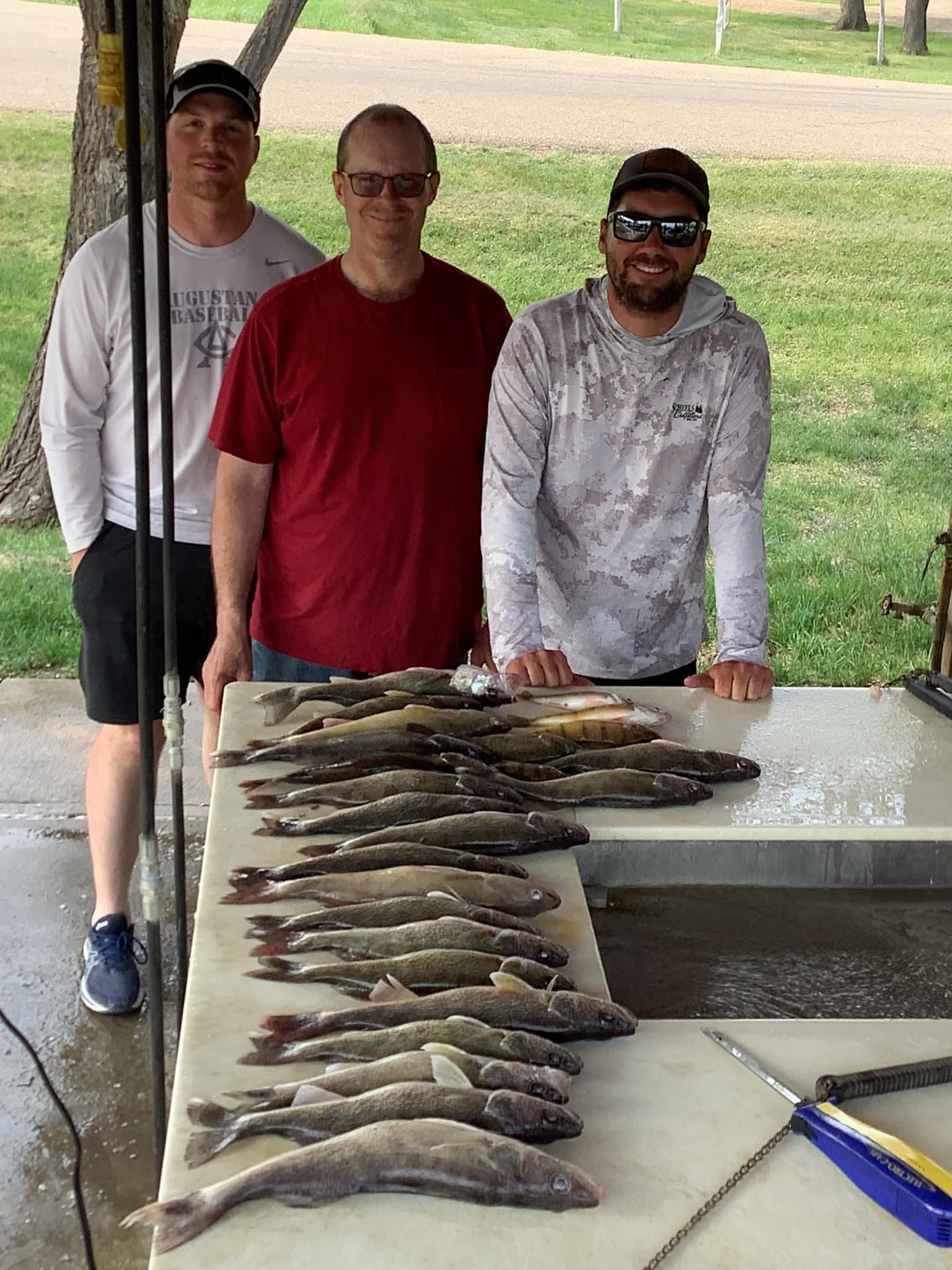 Three men with a catch of fish on a cleaning table outdoors.