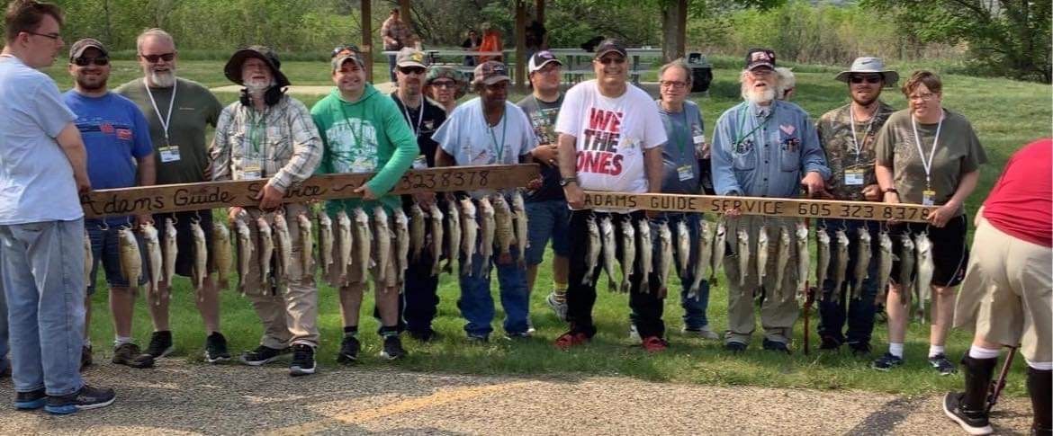 Group of people holding up boards with multiple fish hanging from them outdoors.