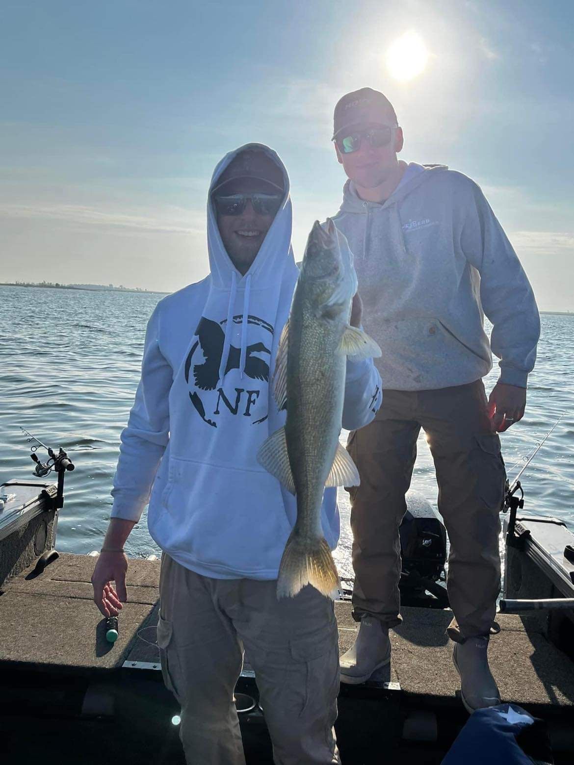Two people on a boat with a fish. One holds the fish, sunny water backdrop.
