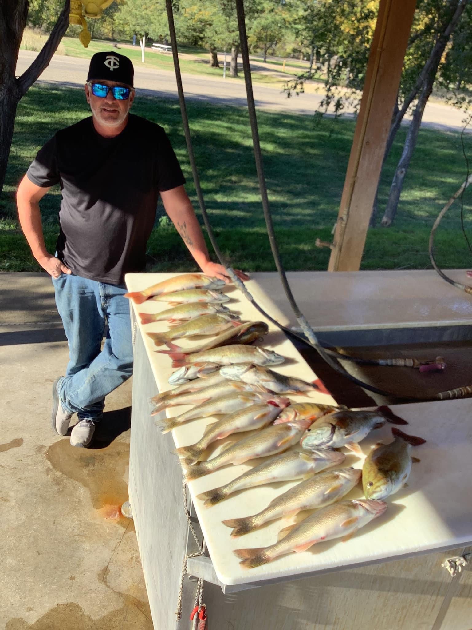 Man leaning on a table displaying many fish; outdoors setting.