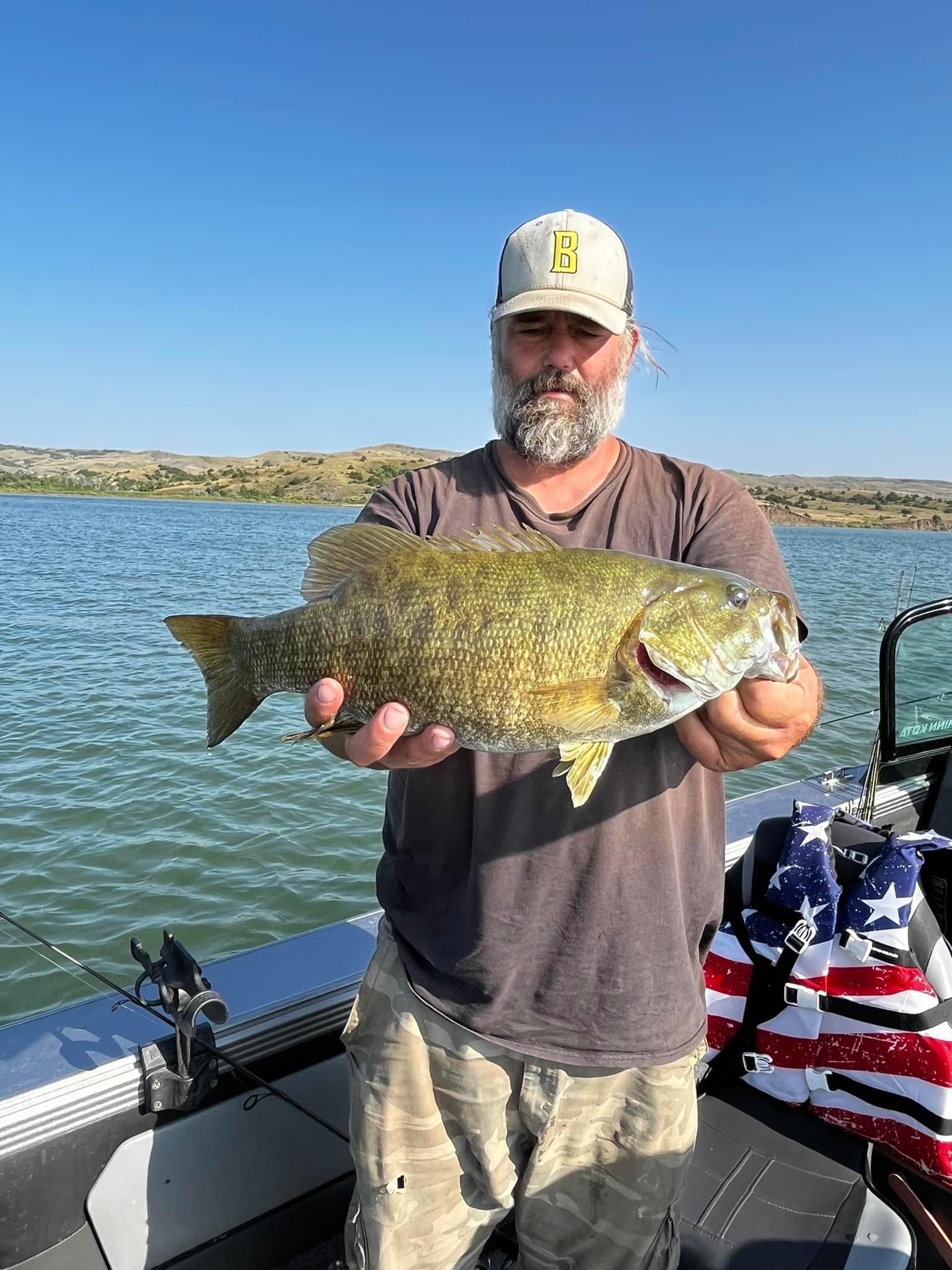 Man holding a large fish on a boat, blue water in background. Sunny day.