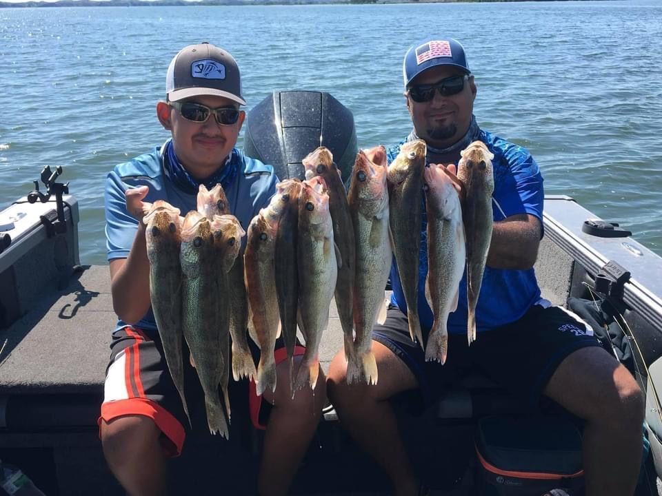 Two people on a boat holding up a large catch of fish, smiling. Sunny day on water.