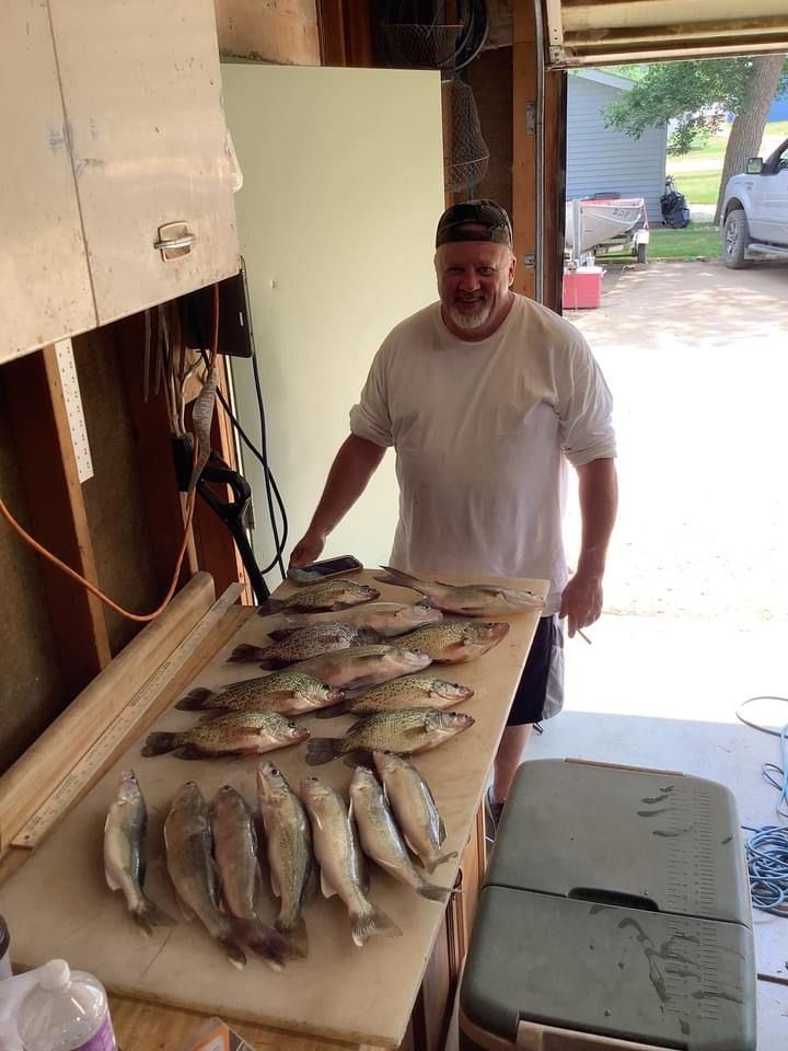 Man smiling next to a table with many fish, possibly cleaned, inside a garage or shed.
