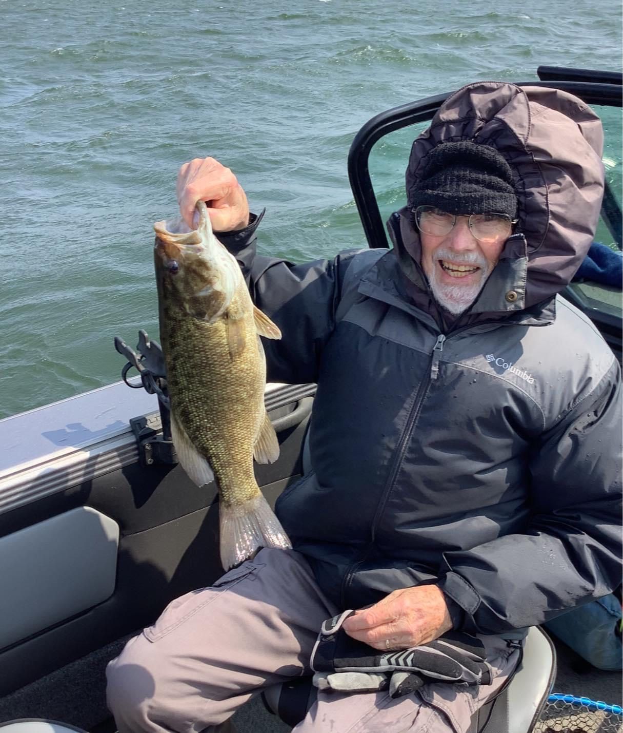 Person in hooded jacket holds up a fish on a boat.