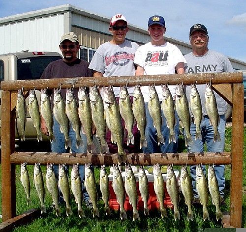 Four men display caught fish hanging on a rack outdoors.