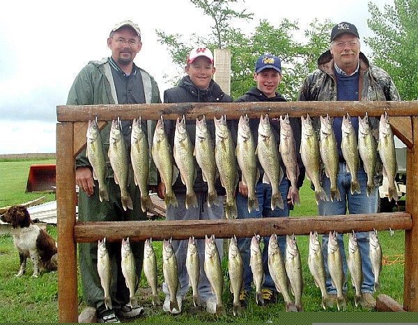 Men and boys with a wooden rack holding many fish, outdoors near a dog.