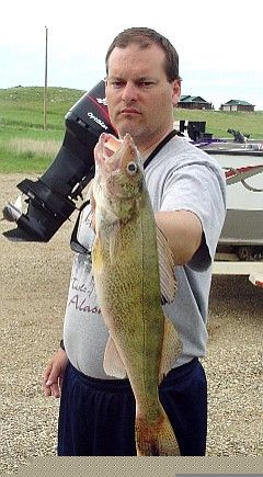 Man holding a walleye fish near a boat, boat motor visible, outdoors.