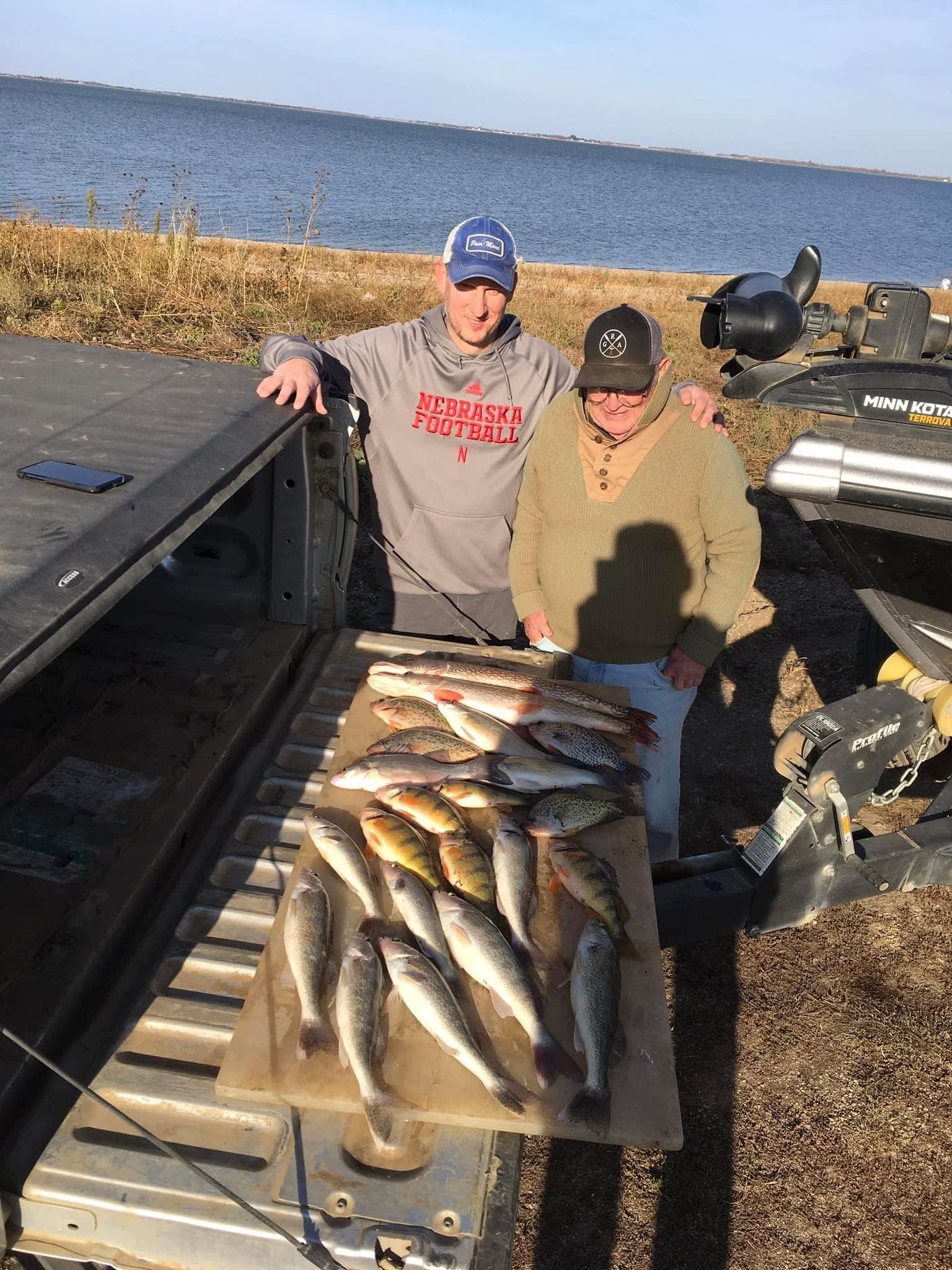 Two men with a fish haul on a truck tailgate near water. Sunny day.