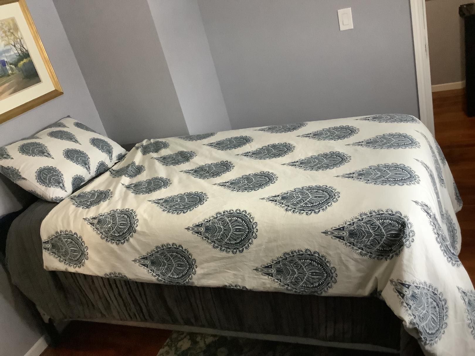 Bed with patterned white and blue paisley comforter and pillow in a gray room.