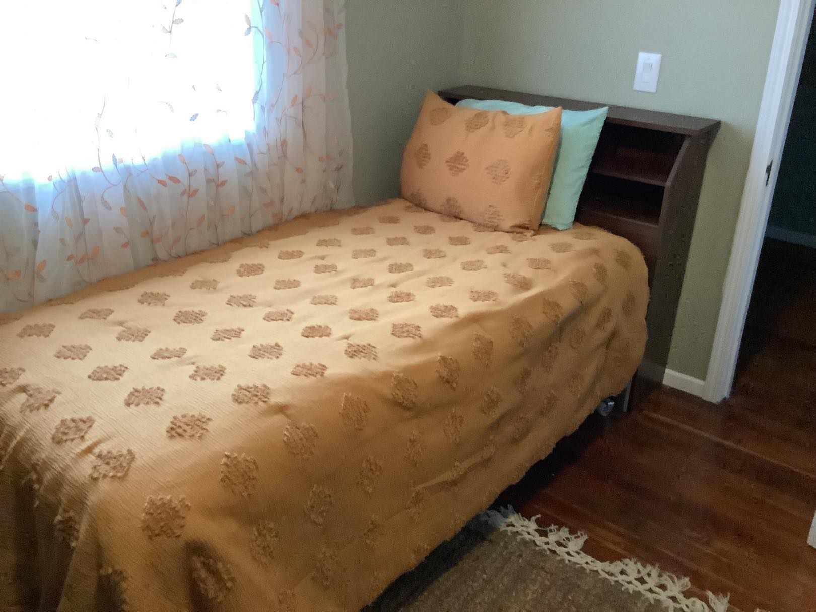 A twin bed with patterned comforter and pillows sits against a wall with a window.