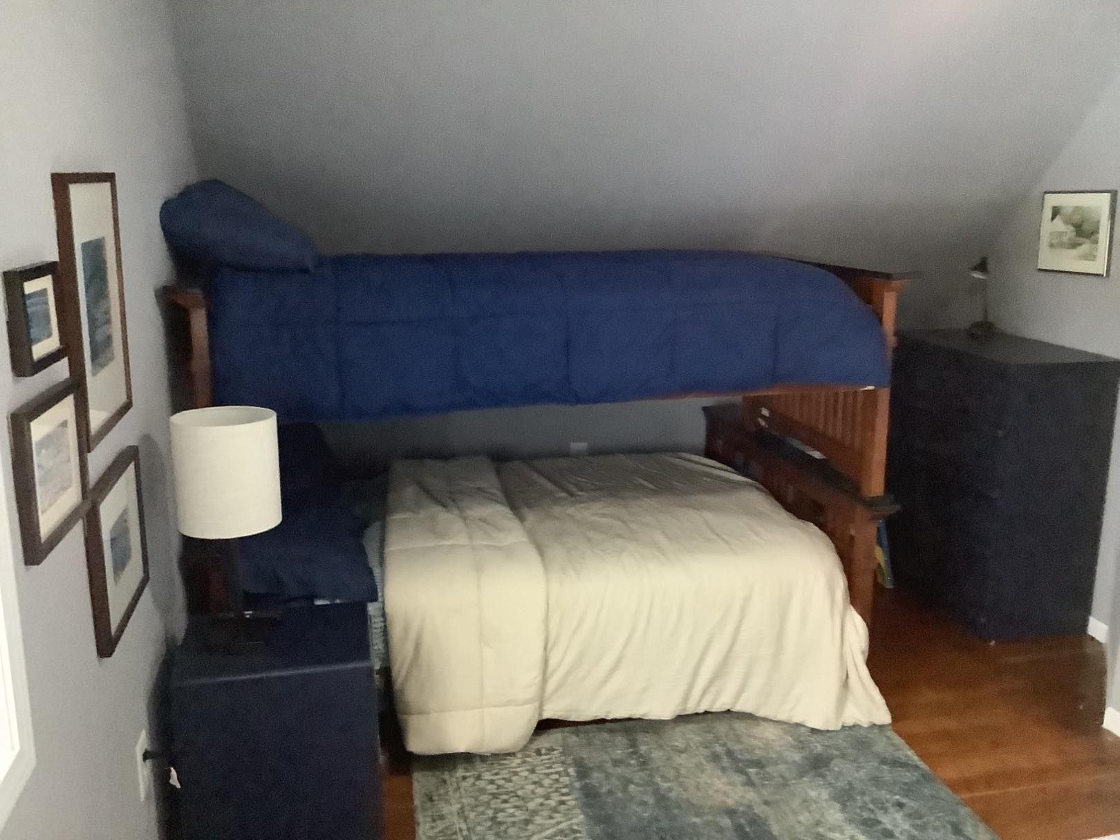 Bunk bed in room with a bottom bed, and a top bed with navy bedding. Nightstand with lamp.