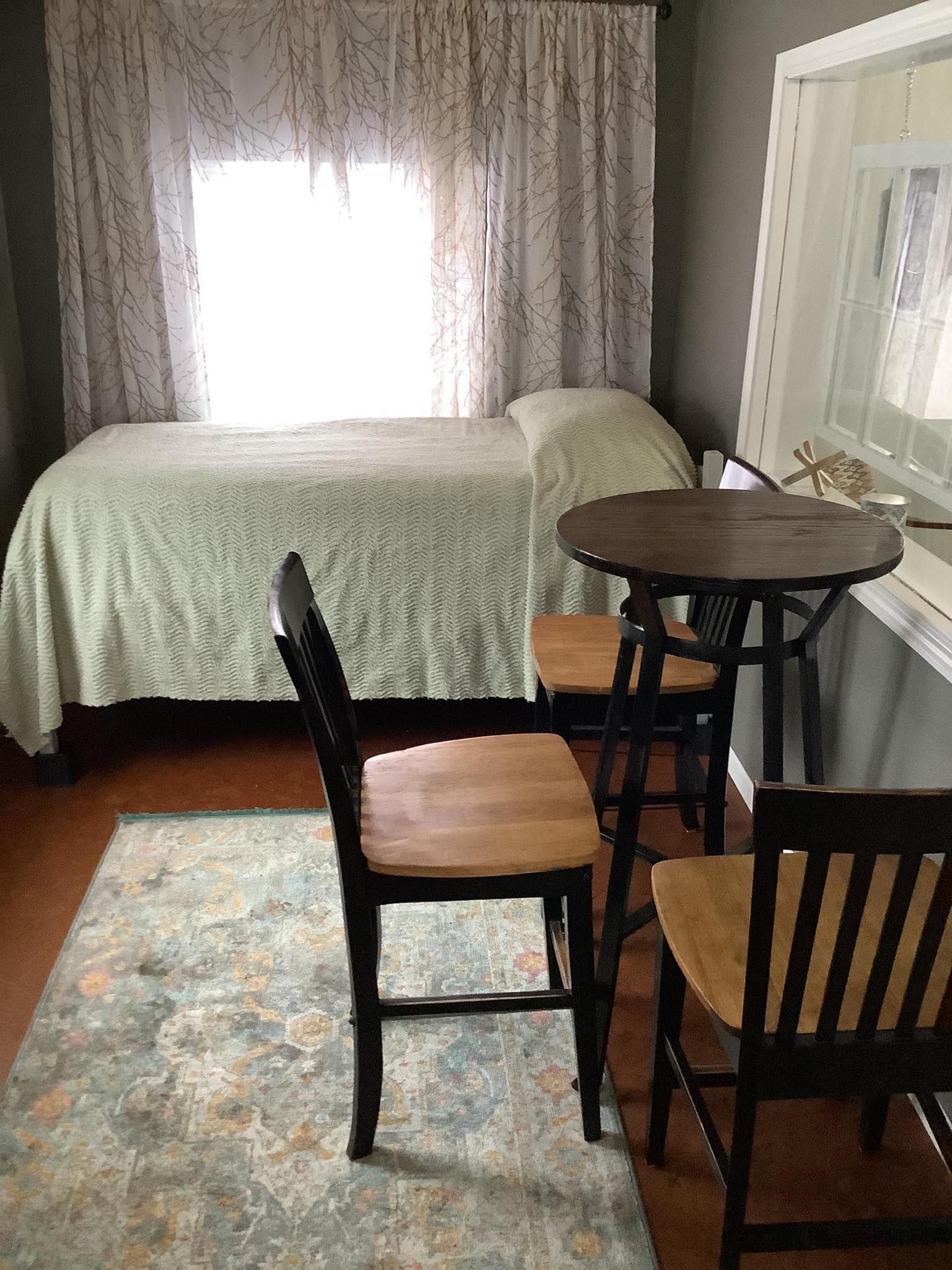 Bedroom with bed, small table with two chairs, and a window with lace curtains.