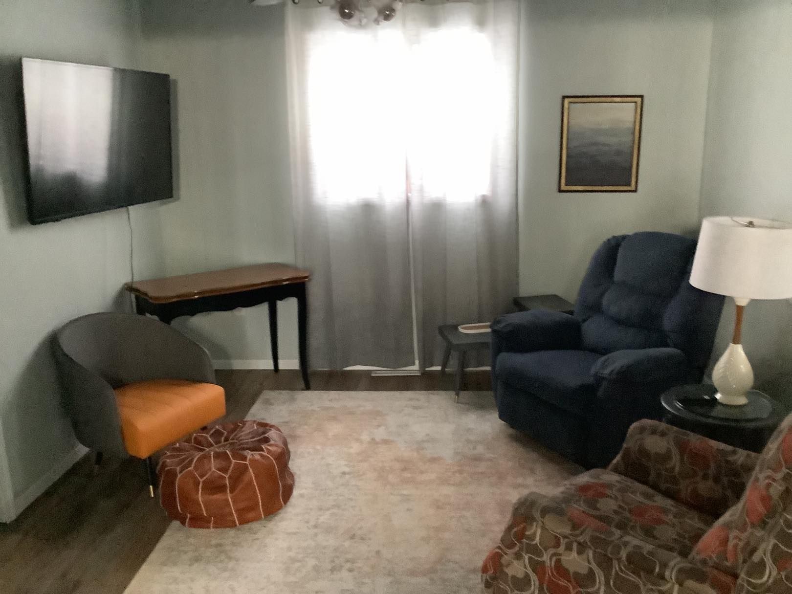 Living room with a TV, chairs, a table, and a window with gray curtains and a light-colored rug.