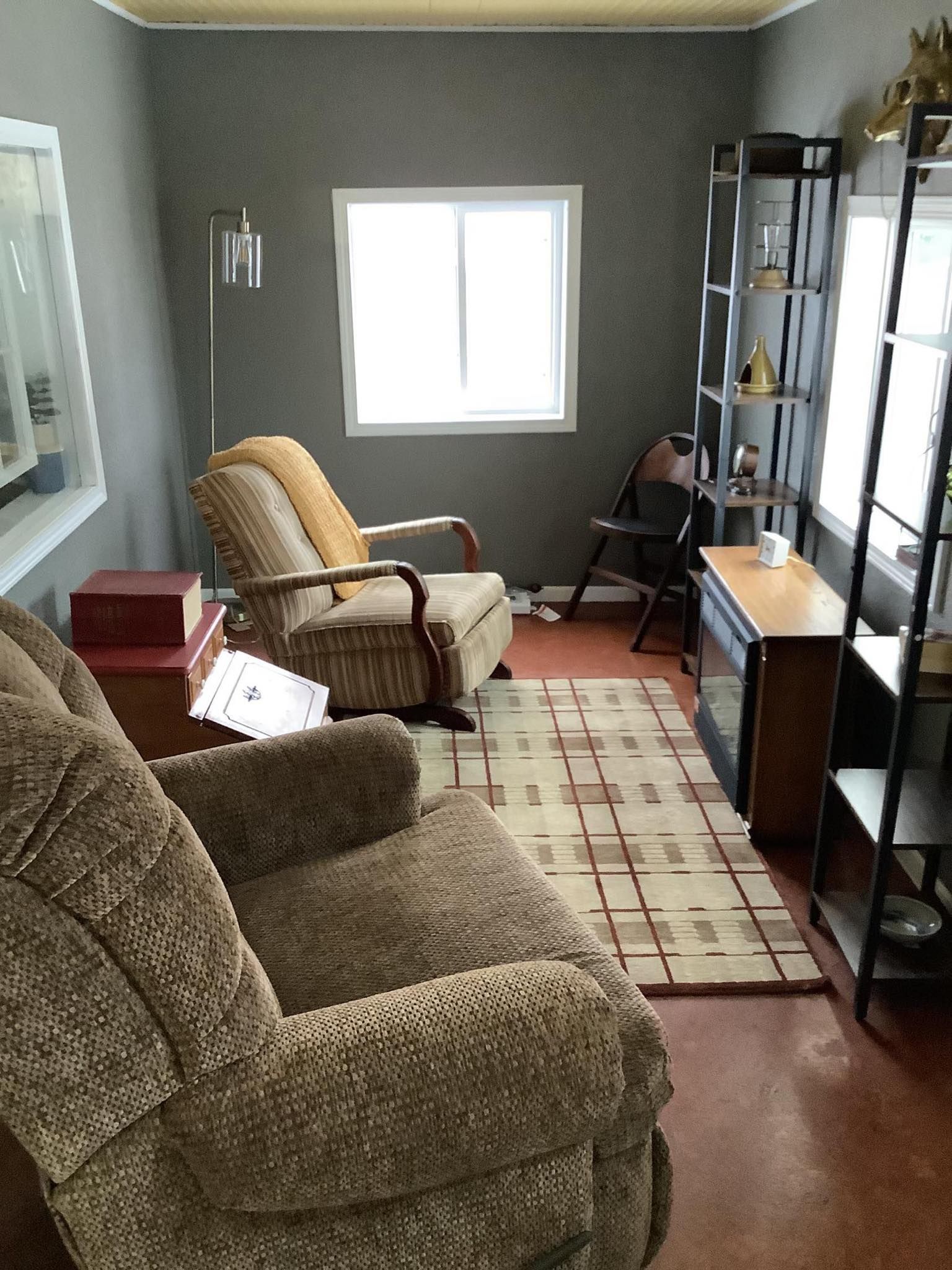 Cozy living room with two recliners, a window, shelving unit, and a patterned rug on a red floor.
