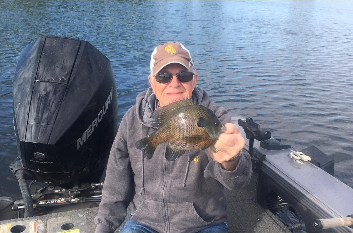 Man in a boat holding a bluegill fish, water and boat motor in the background.