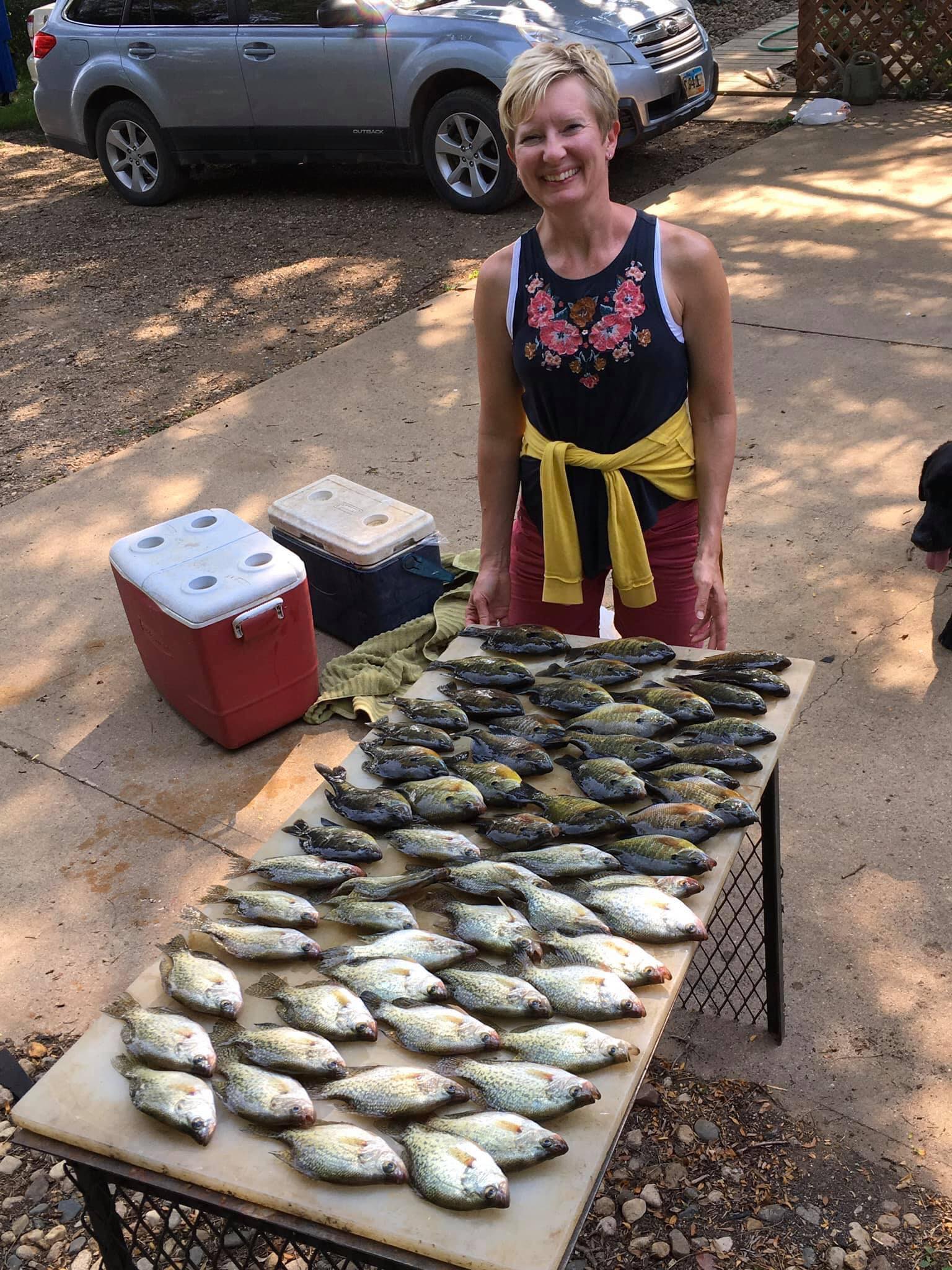 Woman with a large catch of fish on a table; Subaru Outback and RTIC coolers in the background.