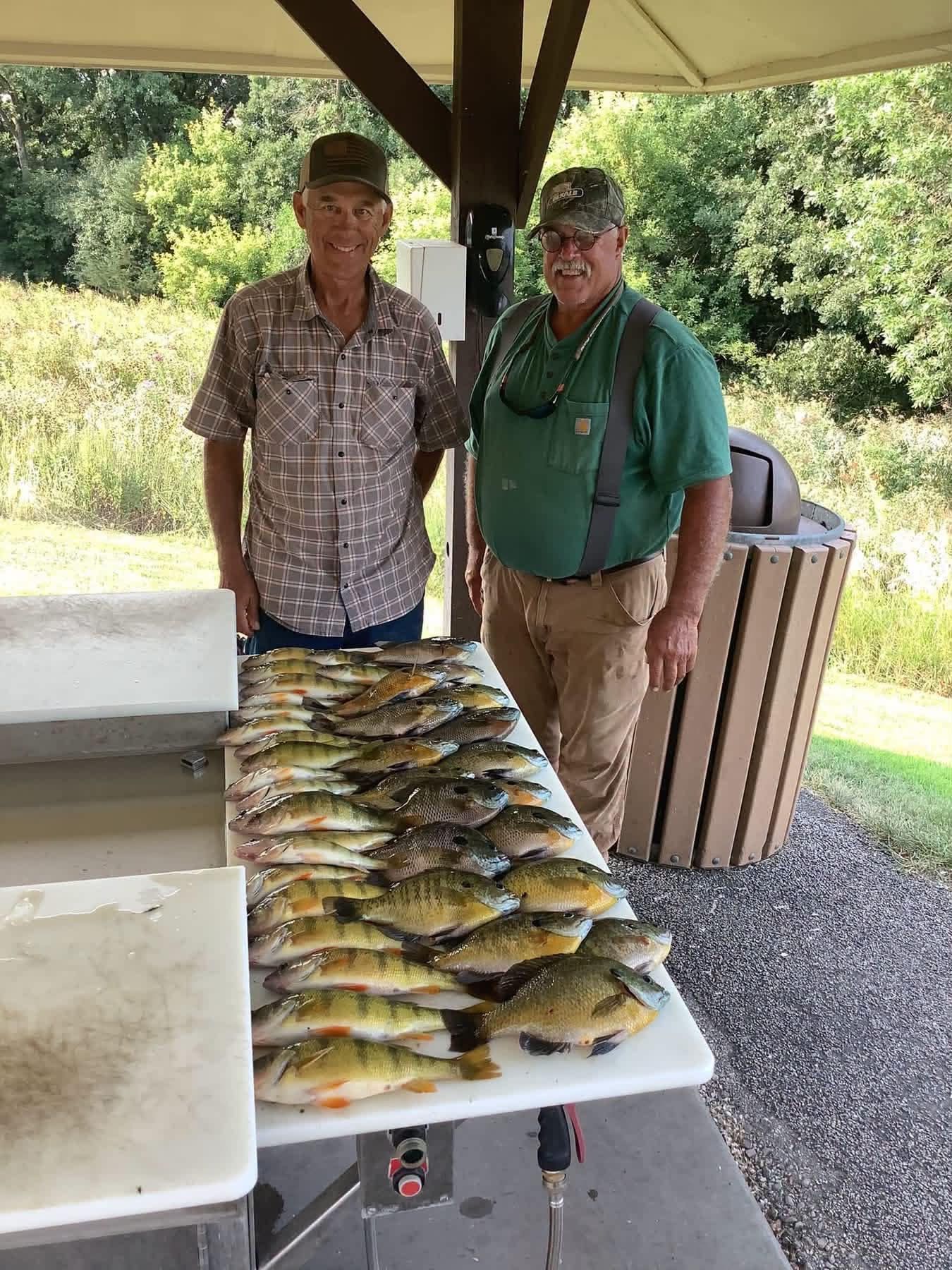 Two people standing beside a table covered with freshly caught fish under a pavilion.