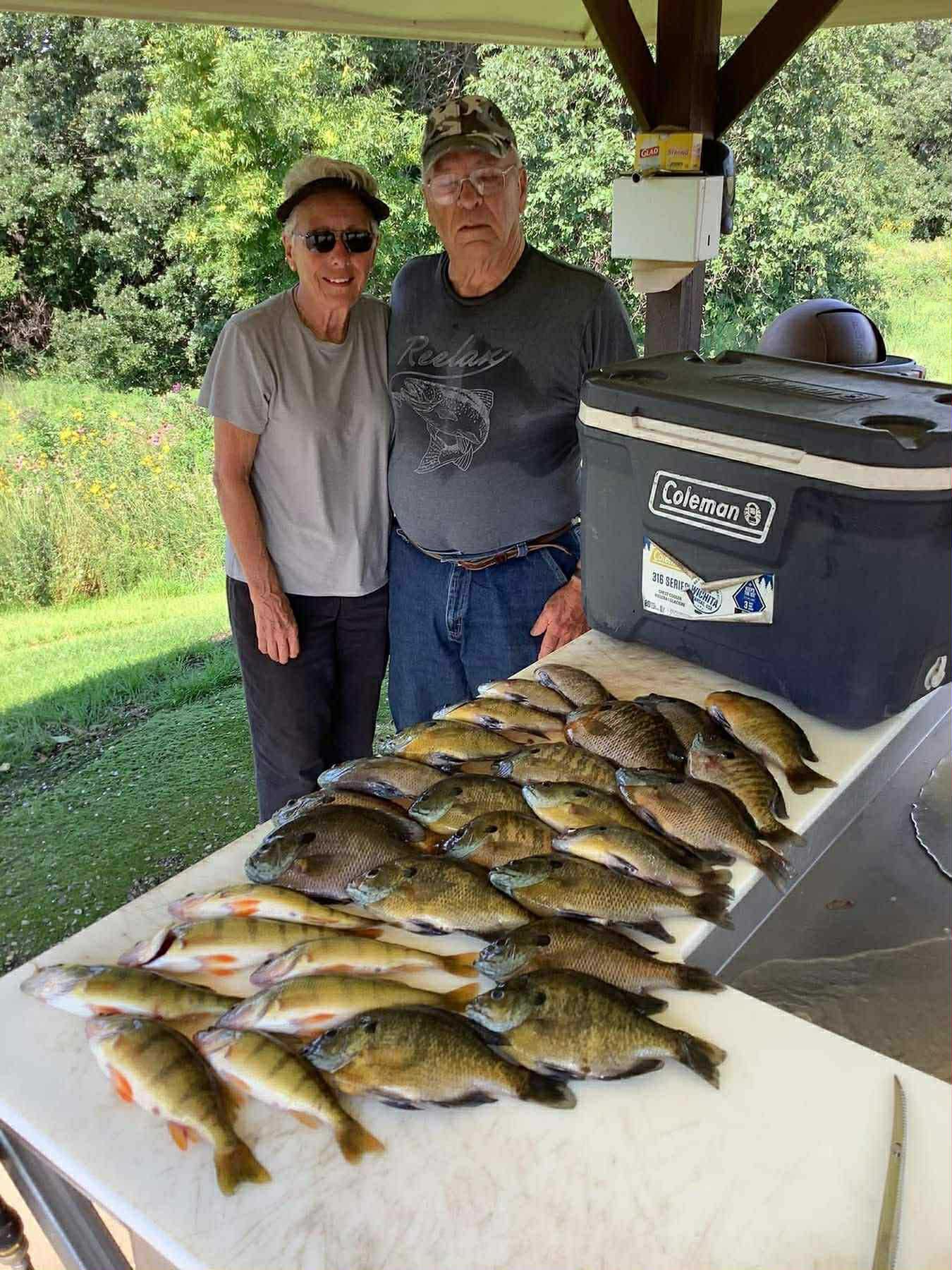 Two people standing by a table with many freshly caught fish, at an outdoor cleaning station.