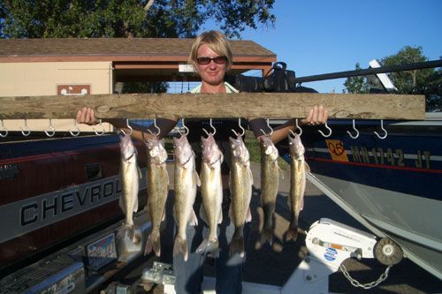 Woman holding a board with multiple fish hooked on it, standing in front of a boat.