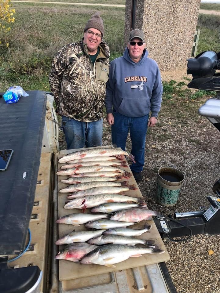 Two men pose with a pile of caught fish on a truck bed.