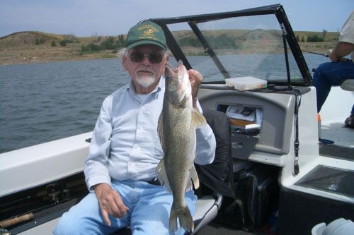 Man in a boat holding a walleye fish; seated on a lake with South Dakota
 hills in the background.