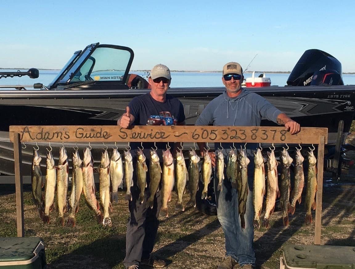 Two men holding a wooden rack of caught fish with a boat in the background. The rack has