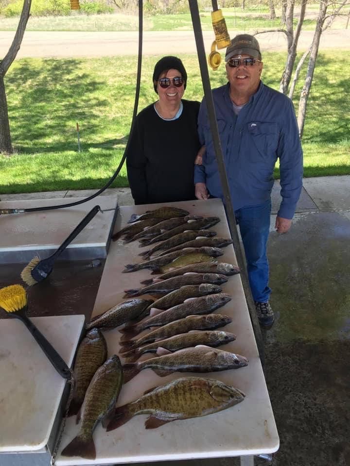 Two people stand behind a table with many fish, likely a fishing catch.