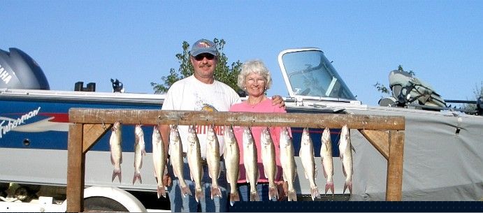 Couple posing with a boat and a rack of fish in front of them under a blue sky.