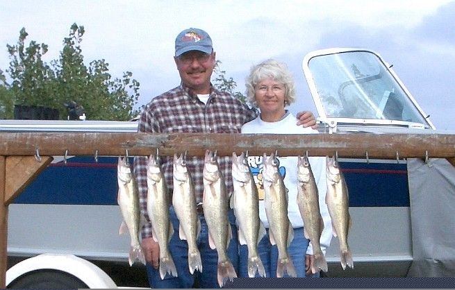 Couple stands behind a rack of fish caught on a boat; they smile.