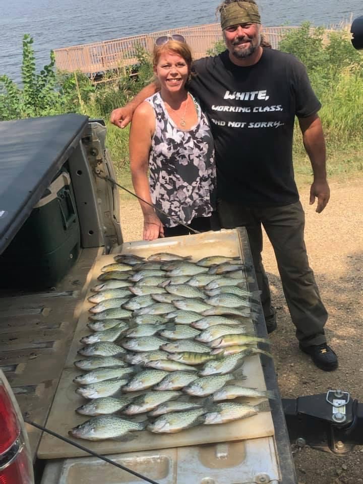 A couple poses with a large catch of fish on the tailgate of a truck, lakeside.