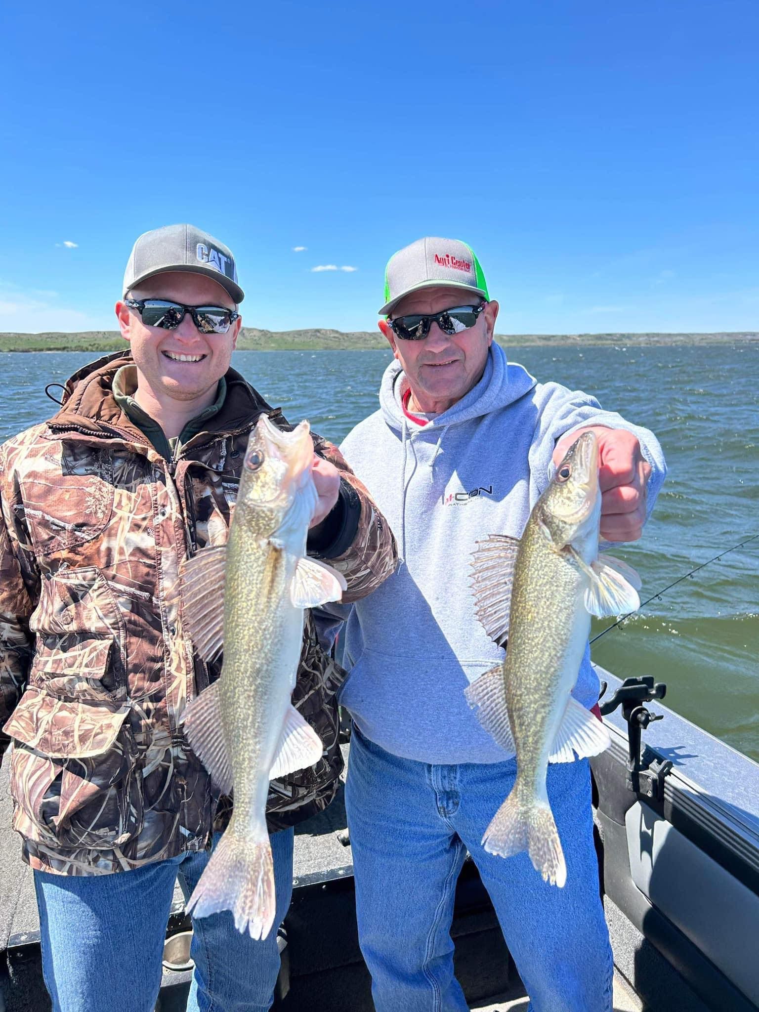 Two people on a boat holding up walleye fish they caught. Bright sunny day, blue sky, and lake water.