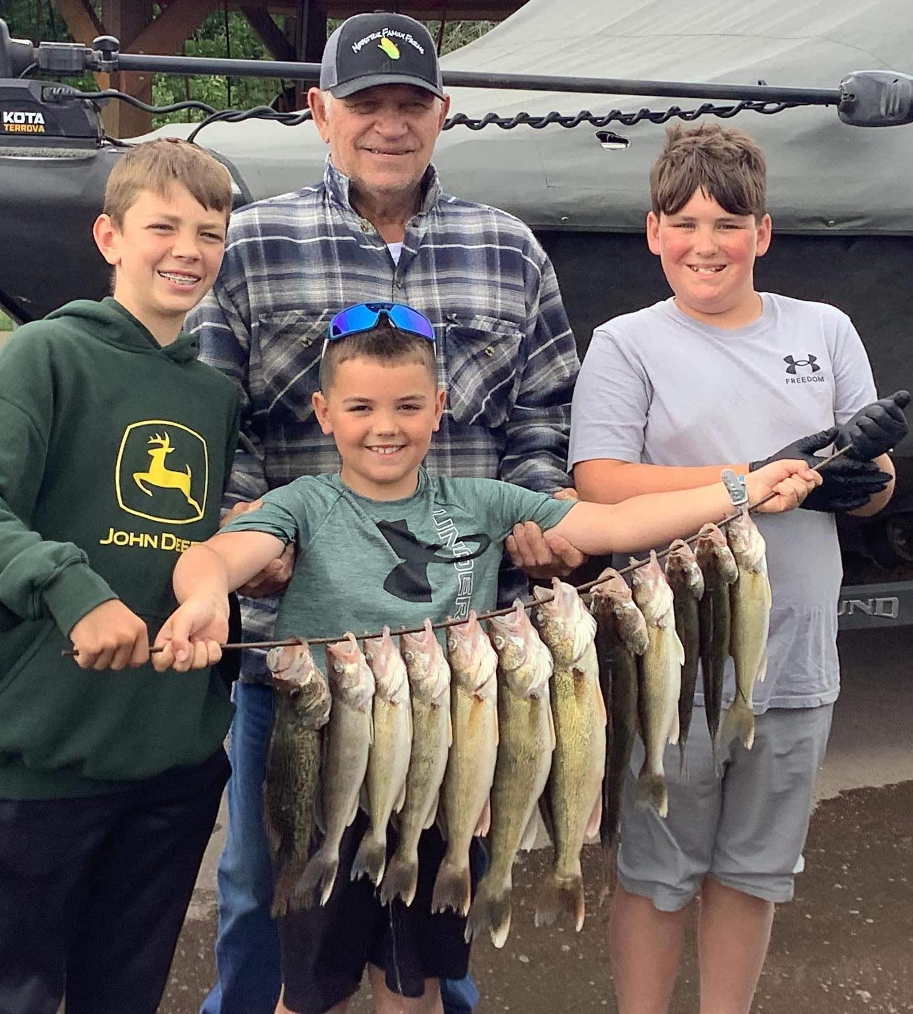 Four people holding up a string of caught fish, smiling. Outdoors, near a Lund Tyee boat.
